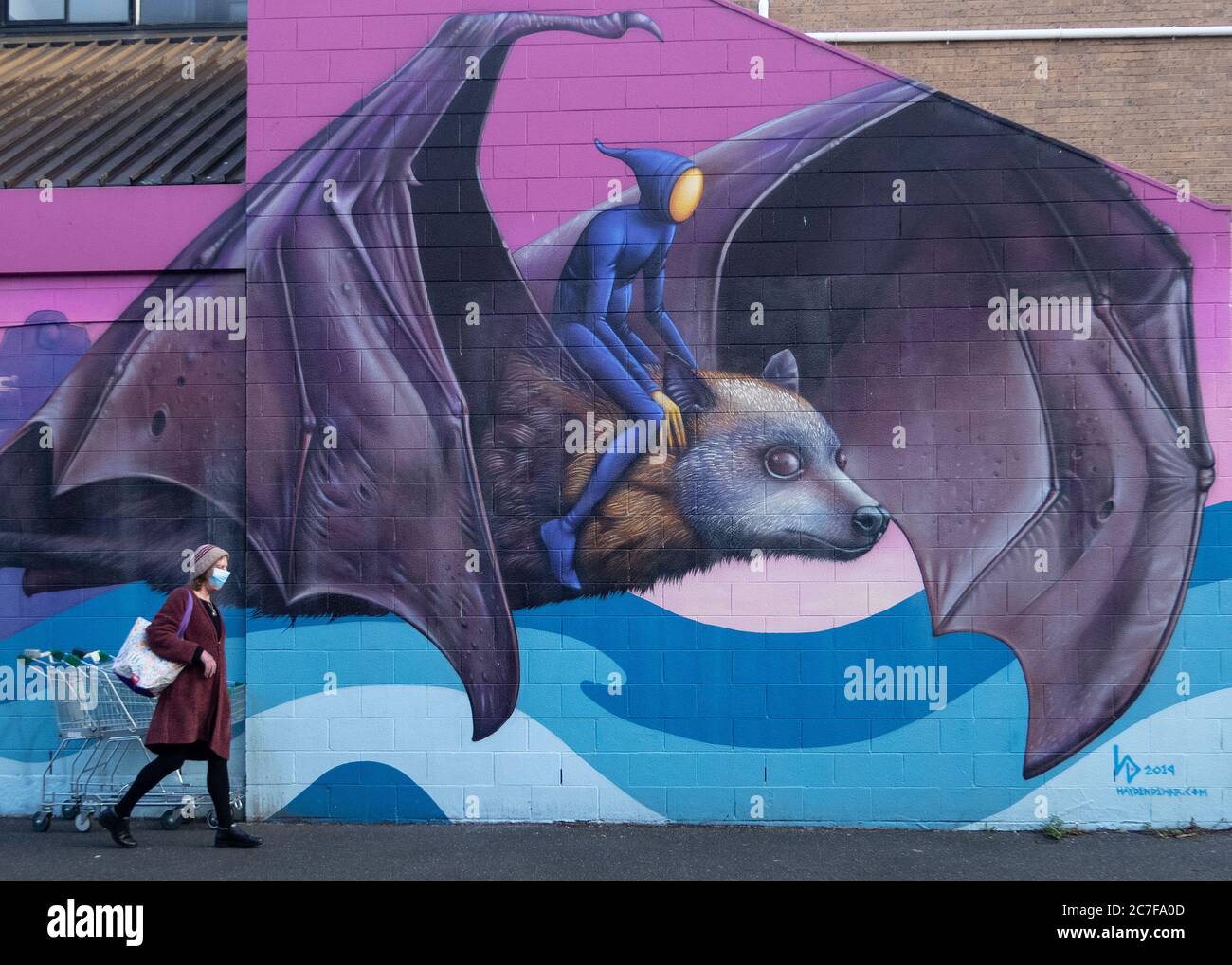 Melbourne Australia Covid-19 pandemia. Una persona che indossa una maschera protettiva passa davanti alla Street art di un pipistrello a Melbourne. Foto Stock