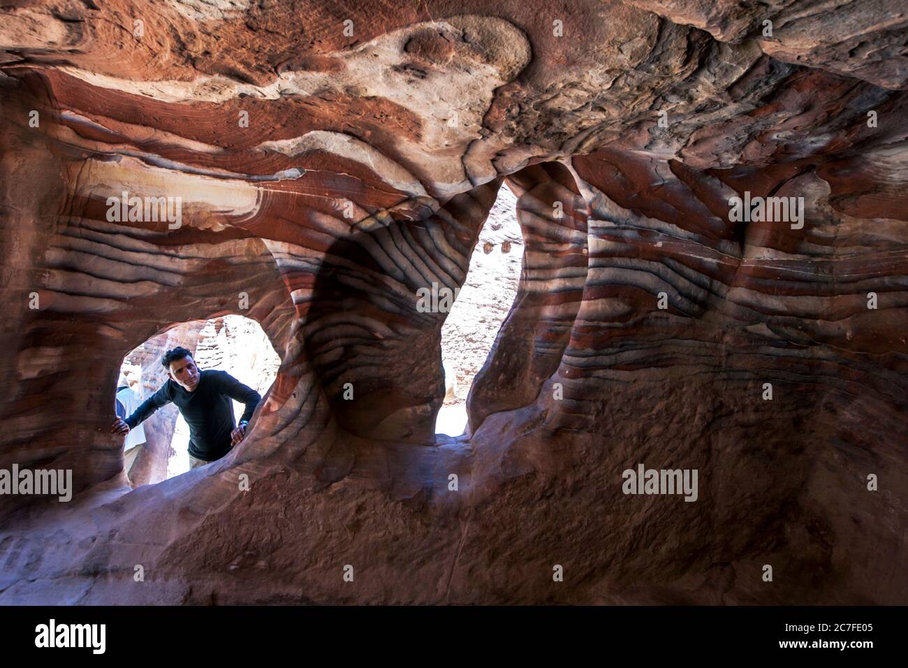 Un uomo che guarda all'interno di una delle spettacolari grotte di arenaria a Petra in Giordania. Petra fu probabilmente fondata già nel 312 a.C. Foto Stock