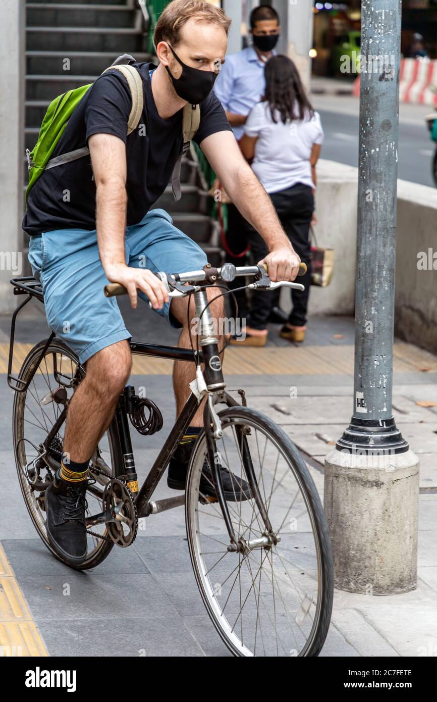 Uomo che indossa una maschera e che cavalca una bicicletta durante la pandemia del covid 19, Bangkok, Thailandia Foto Stock