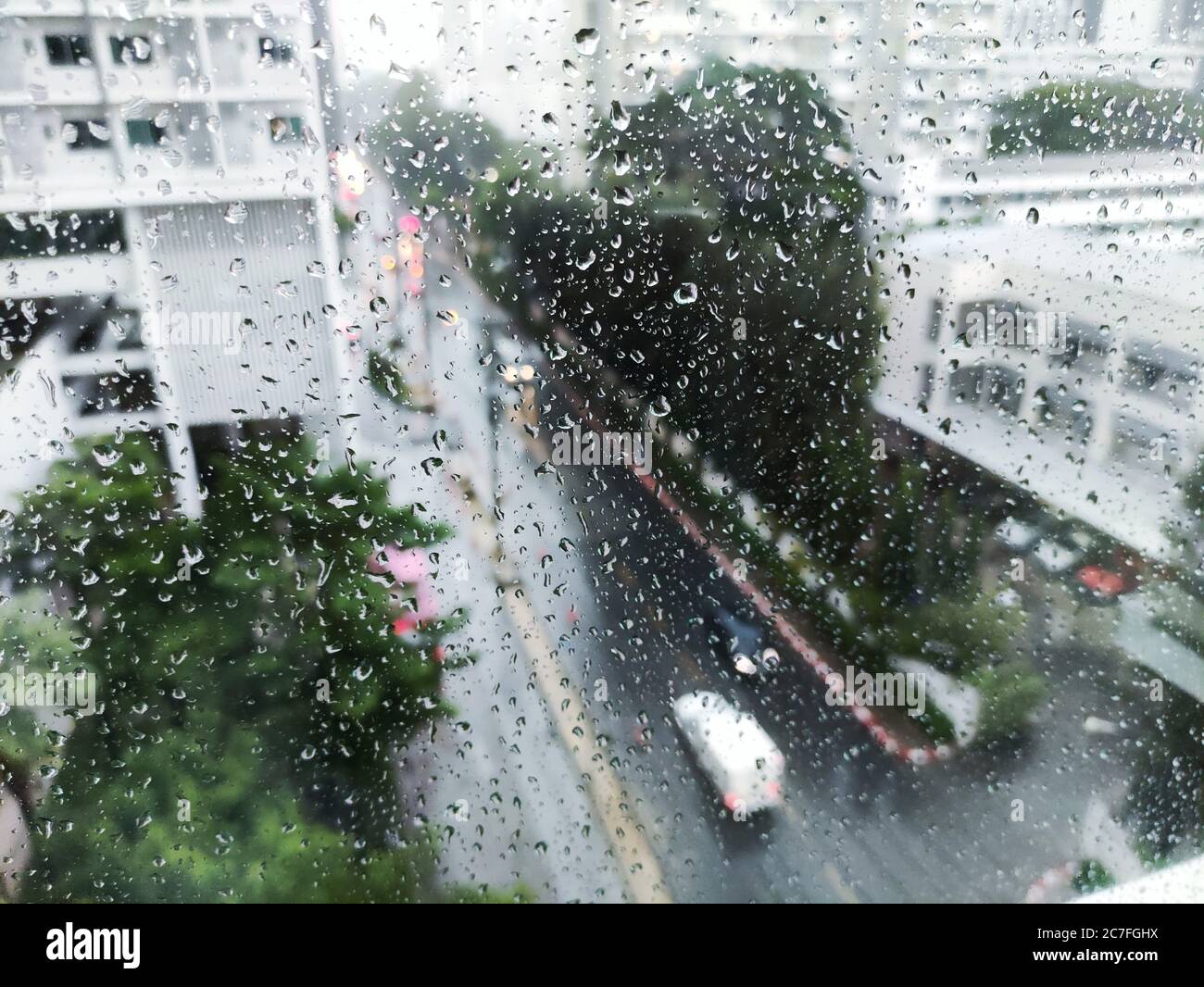 piovendo sulla strada, vista aerea. goccia d'acqua catturata sulla finestra di vetro dell'appartamento. guardando giù sulla strada durante la tempesta. strada bagnata e guida attenta co Foto Stock