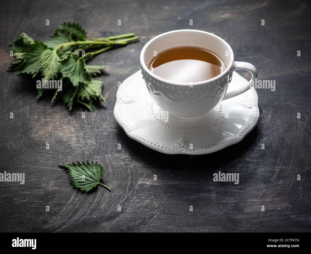 Tè fresco di ortica in tazza di ceramica bianca su tavolo in legno d'epoca. Foto Stock