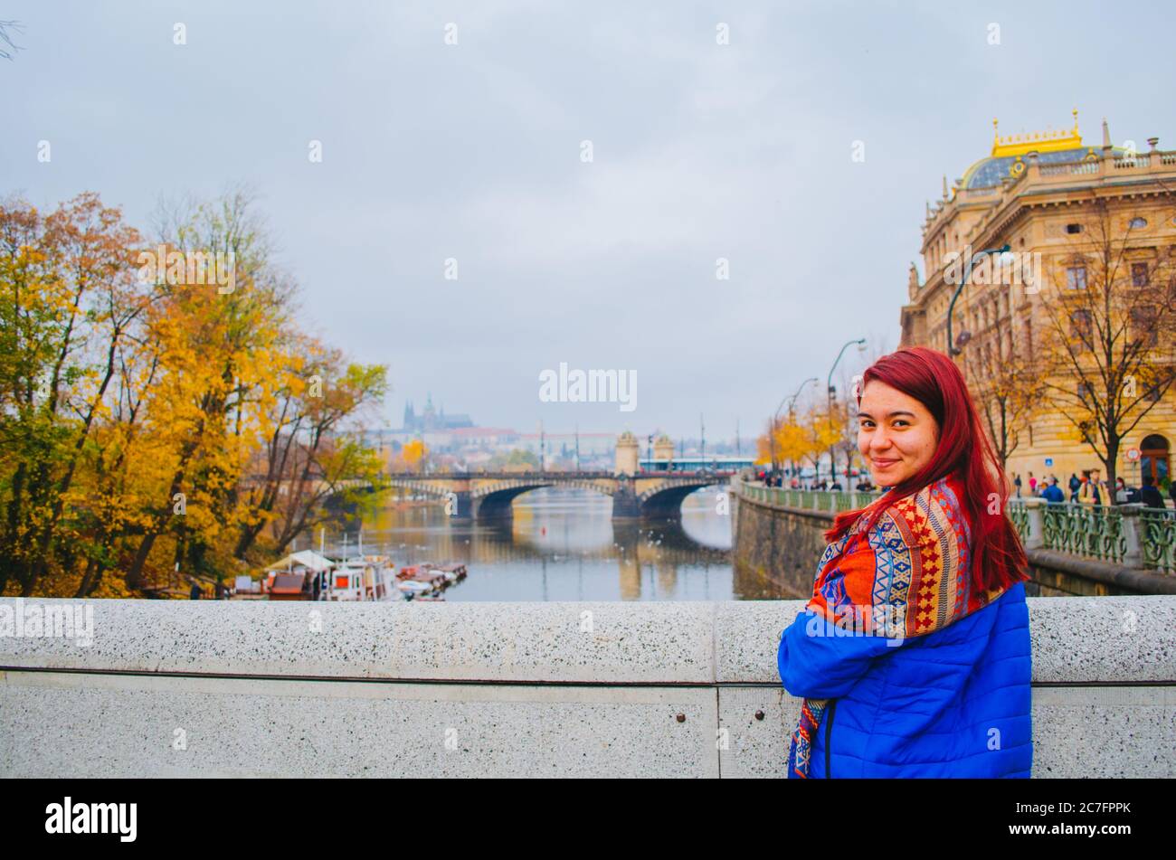 Una donna brasiliana rossa nei suoi 20 davanti ad un ponte a Praga, in Czechia e sorridendo alla macchina fotografica. Foto Stock