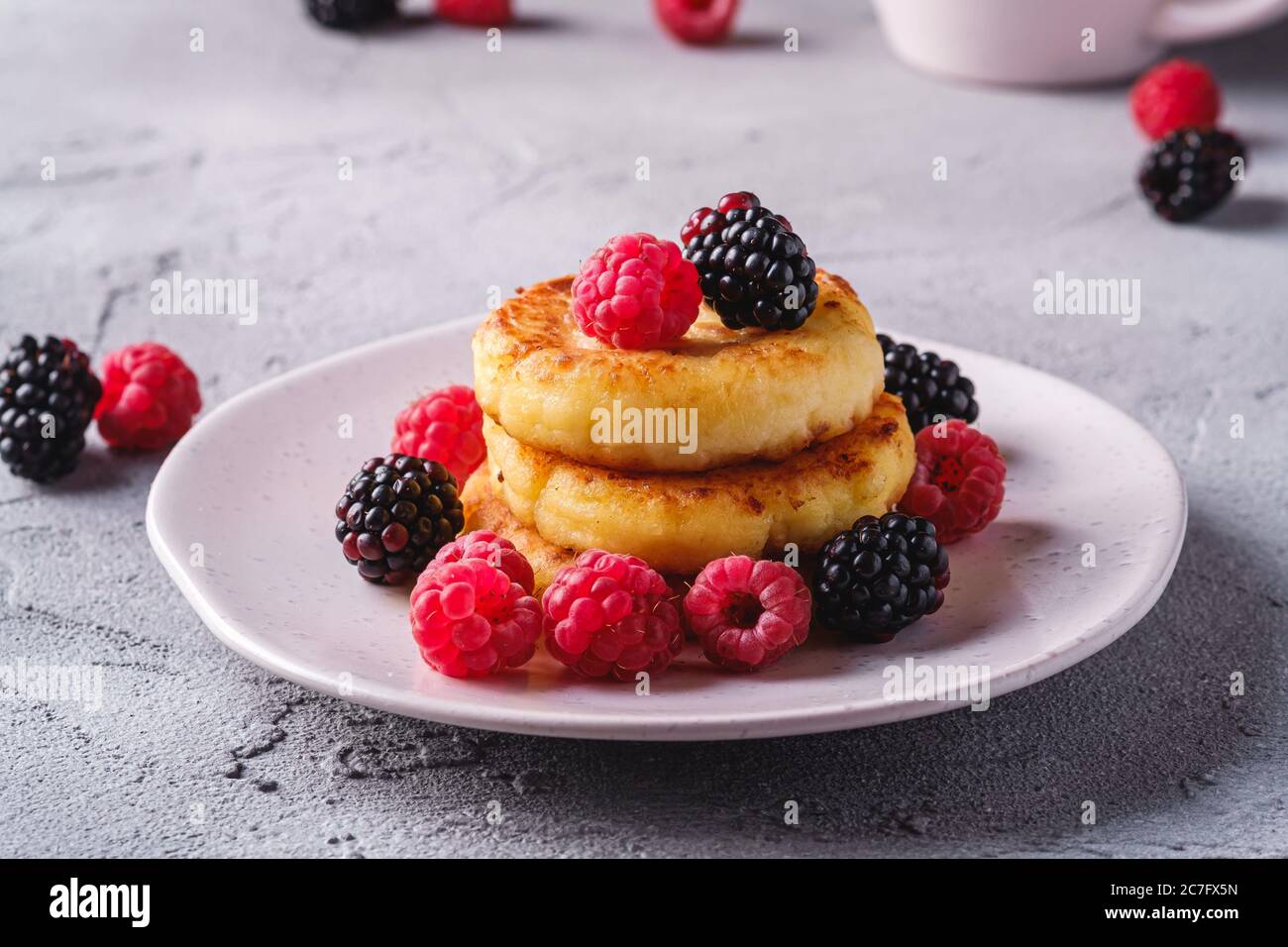 Frittelle al formaggio di cottage, frittelle di cagliata dessert con lampone e frutti di mora in piastra su fondo di pietra in cemento, macro angolo vista Foto Stock