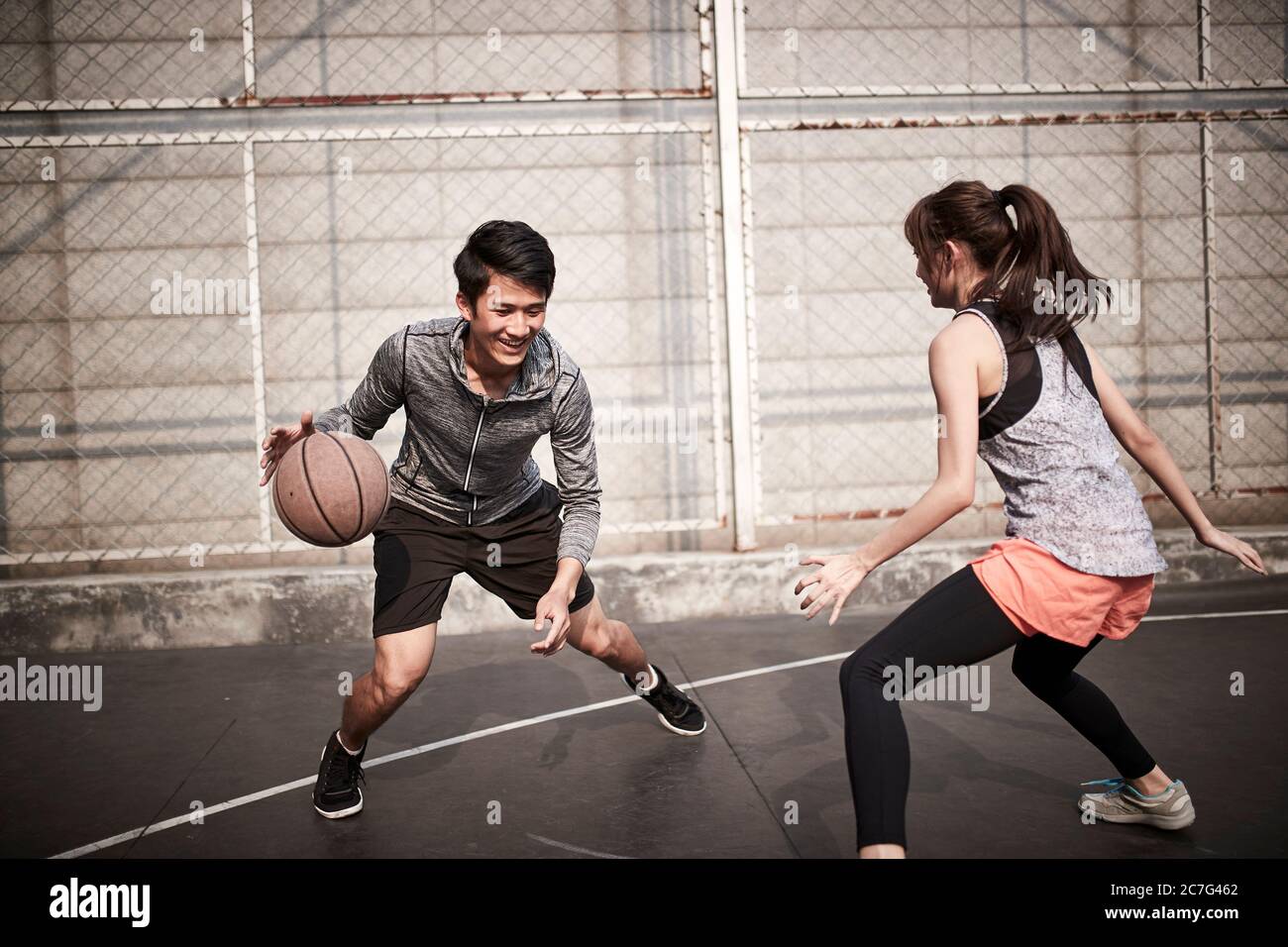 giovane uomo adulto asiatico e donna che si divertono giocando a basket su un campo all'aperto Foto Stock