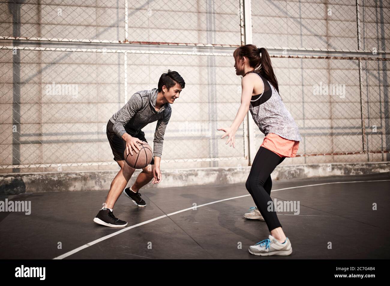 giovane uomo adulto asiatico e donna che si divertono giocando a basket su un campo all'aperto Foto Stock