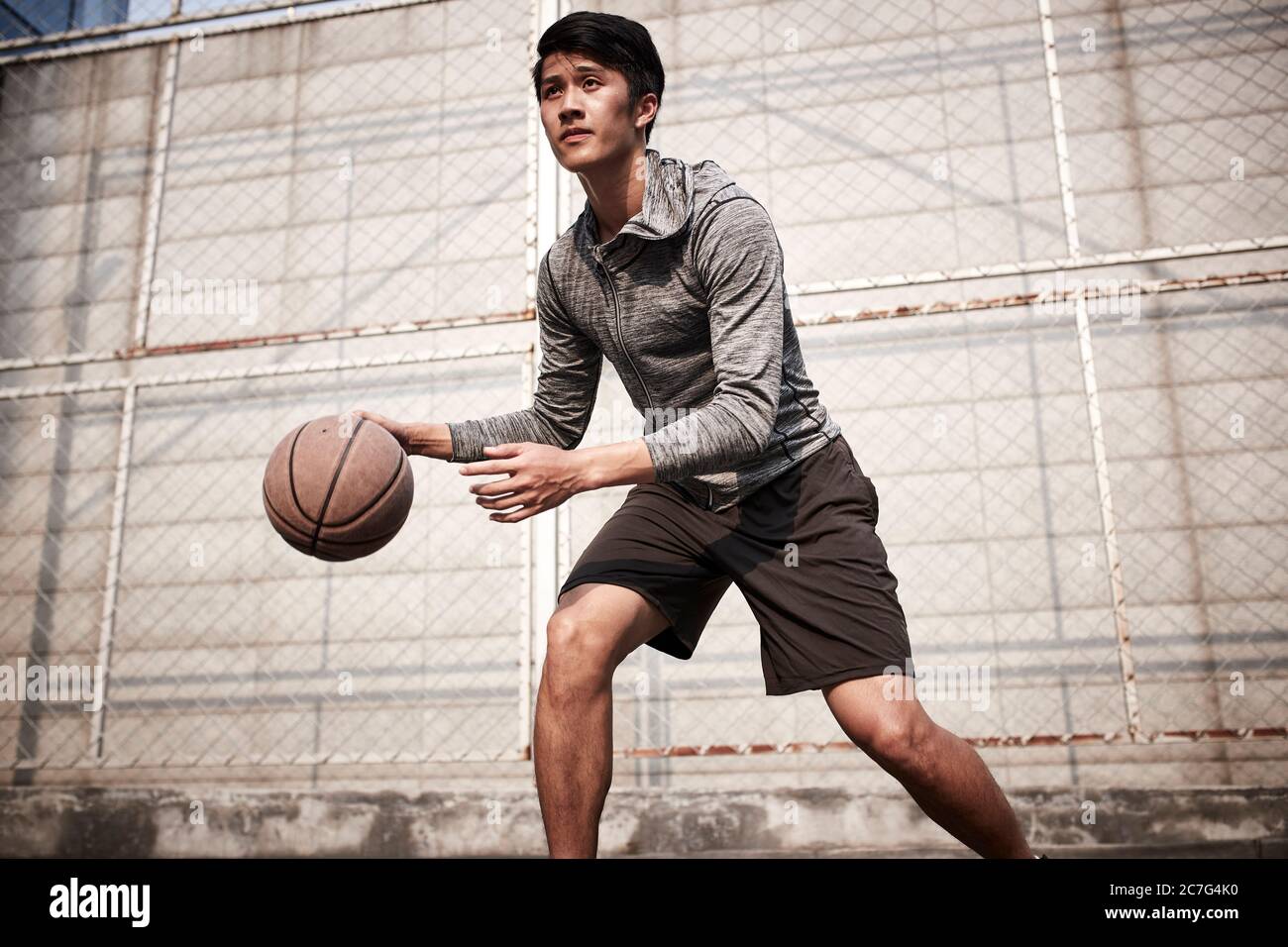 giovane giocatore asiatico di pallacanestro maschile pratica palla abilità di manipolazione sul campo all'aperto Foto Stock