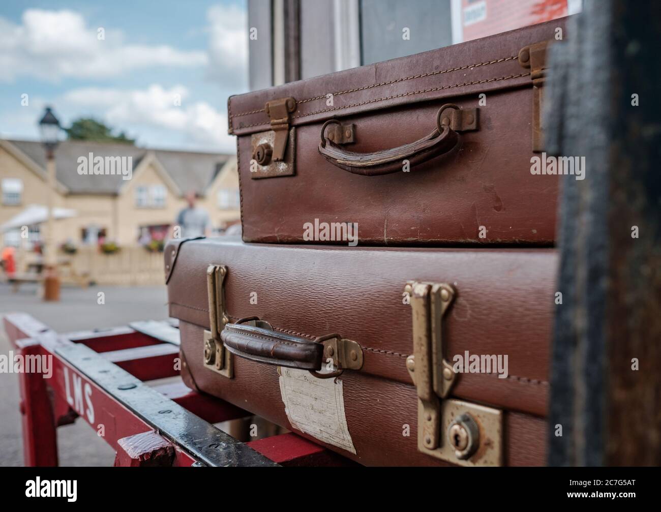 Vista ravvicinata e poco profonda delle valigie in stile vintage caricate su un trolly del periodo del vapore situato in una stazione ferroviaria britannica del periodo. Foto Stock