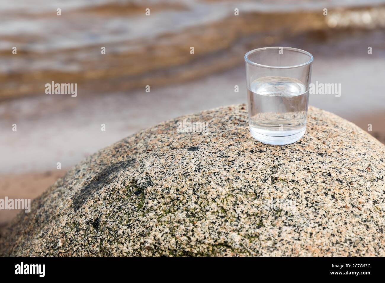 Un bicchiere di acqua potabile si trova sulla pietra costiera. Primo piano con la messa a fuoco morbida selettiva Foto Stock