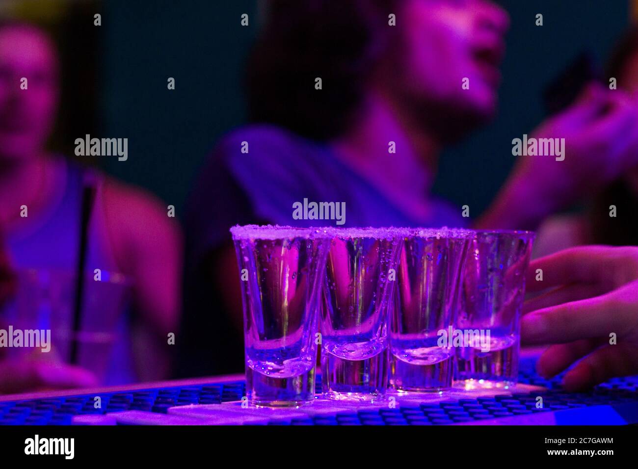 Foto di tequila sul tavolo da bar durante la festa notturna, persone sullo sfondo, foto piene di alcolici con luce LED blu nel night club di Tbilisi. Foto Stock