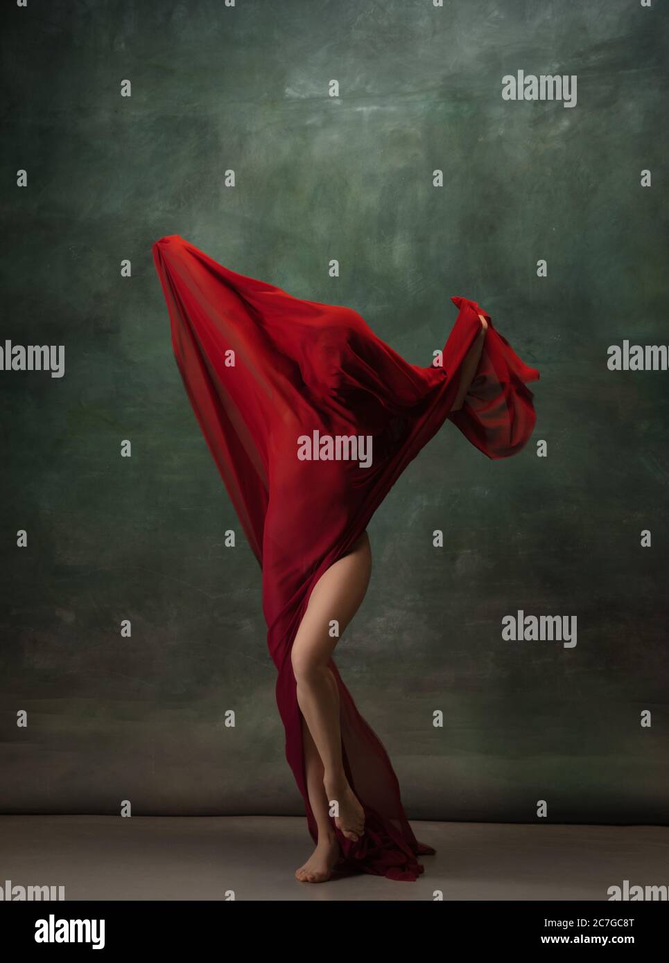 Ali che volano. Ballerina classica e graziosa che balla su sfondo scuro dello studio. Panno rosso profondo. Il concetto di grazia, artista, movimento, azione e movimento. Aspetto senza peso, flessibile. Moda, stile. Foto Stock