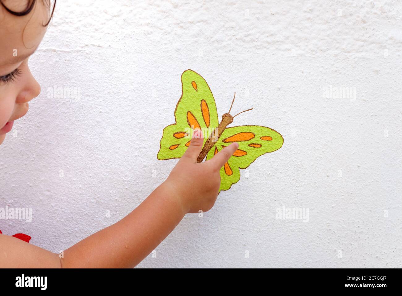 Ragazza che punta il dito su un disegno di una farfalla dipinta sulla parete bianca Foto Stock