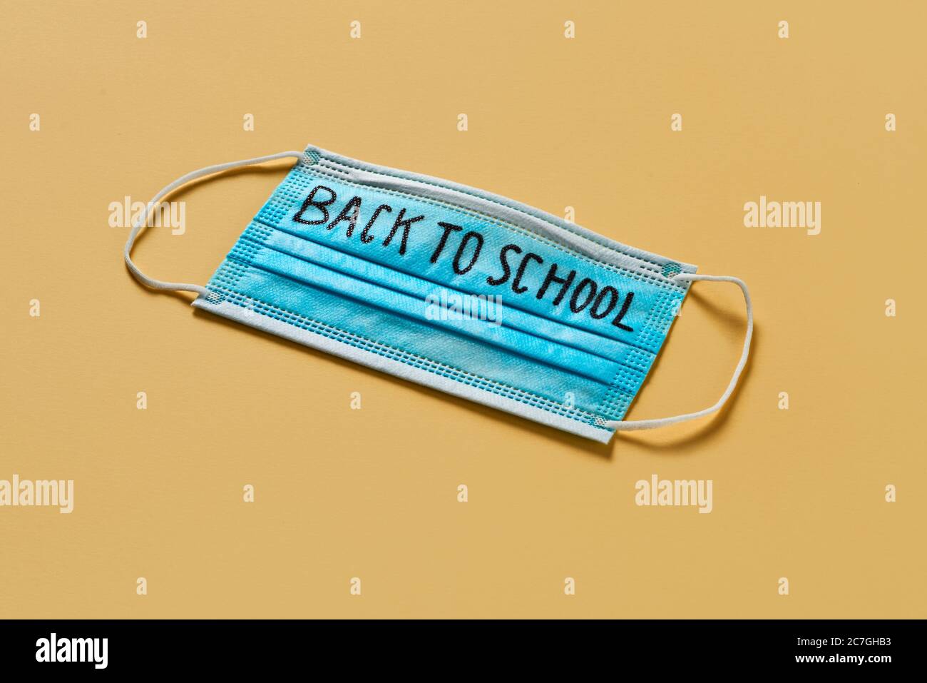 una maschera chirurgica blu con il testo di ritorno a scuola scritto in esso, su uno sfondo giallo, che raffigura la necessità di prevenire l'infezione a scuola nel Foto Stock