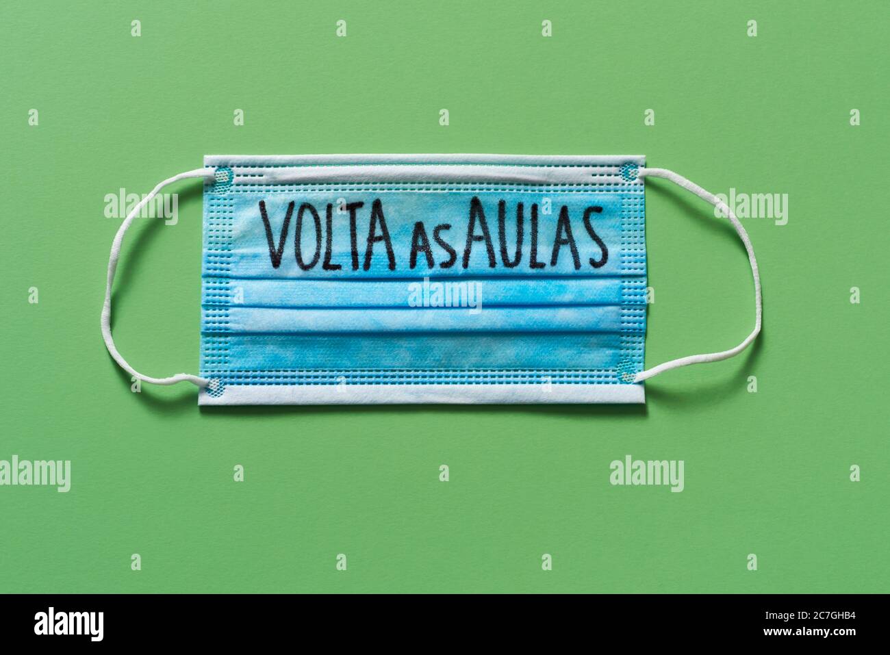 vista ad alto angolo di una maschera chirurgica con il testo di ritorno a scuola scritto in portoghese, su sfondo verde, che raffigura la necessità di prevenire l'infezione Foto Stock
