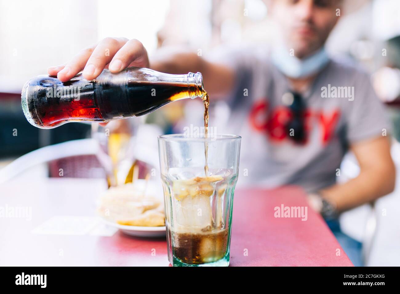 Un uomo con maschera versa una bevanda alla cola in un bicchiere Foto Stock