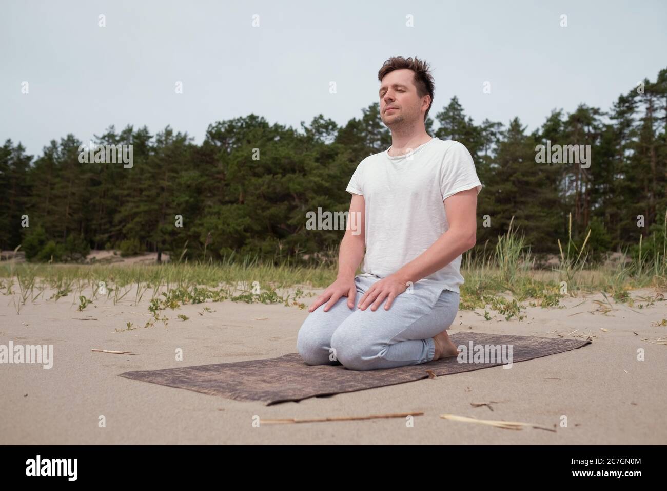 Giovane caucasico che si prepara per la pratica di yoga sulla spiaggia Foto Stock