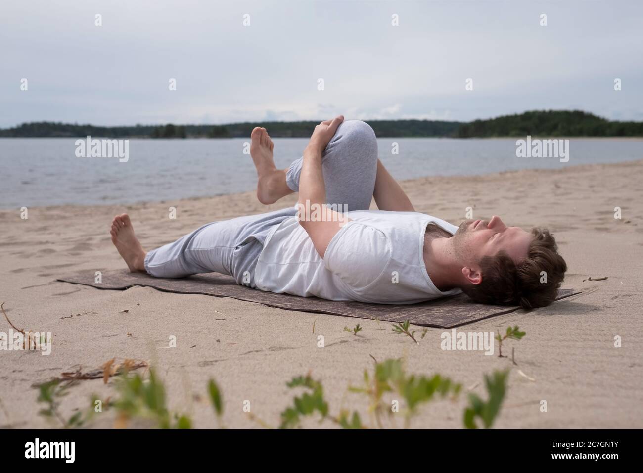 Giovane praticante yoga pavanamuktasana all'aperto sulla spiaggia Foto Stock