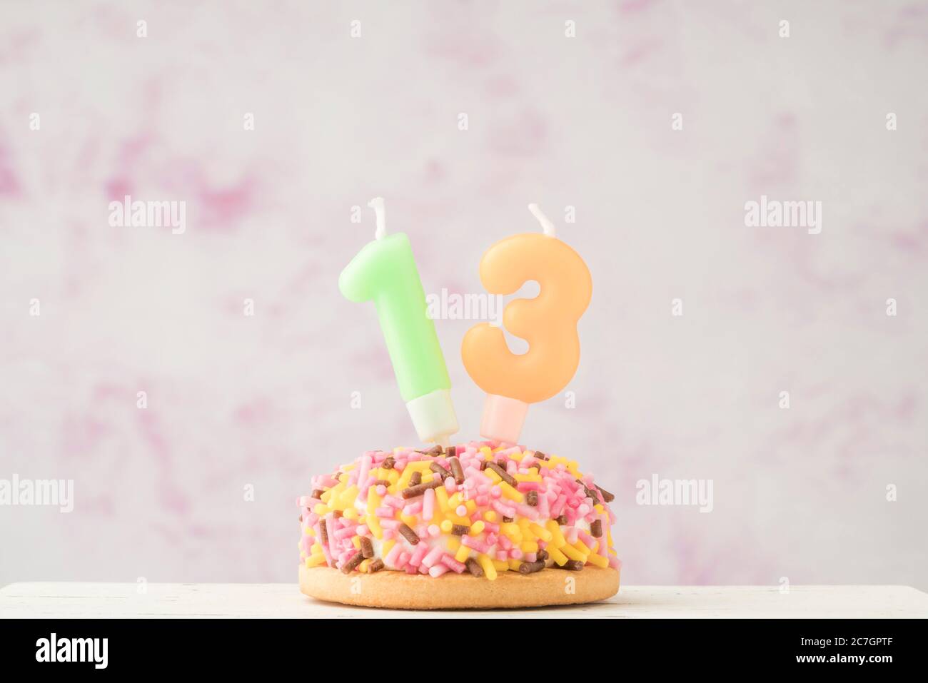 una piccola cupcake colorata con una candela a forma di tredici numeri per la celebrazione del compleanno Foto Stock