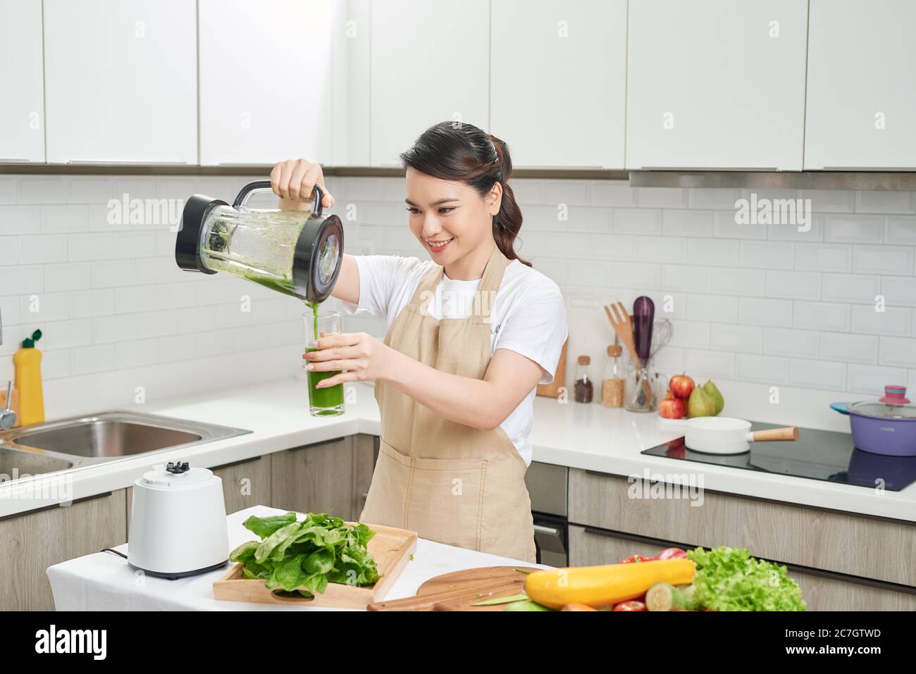 Donna felice sulla dieta detox, versando cocktail verde dal miscelatore in vetro in cucina Foto Stock
