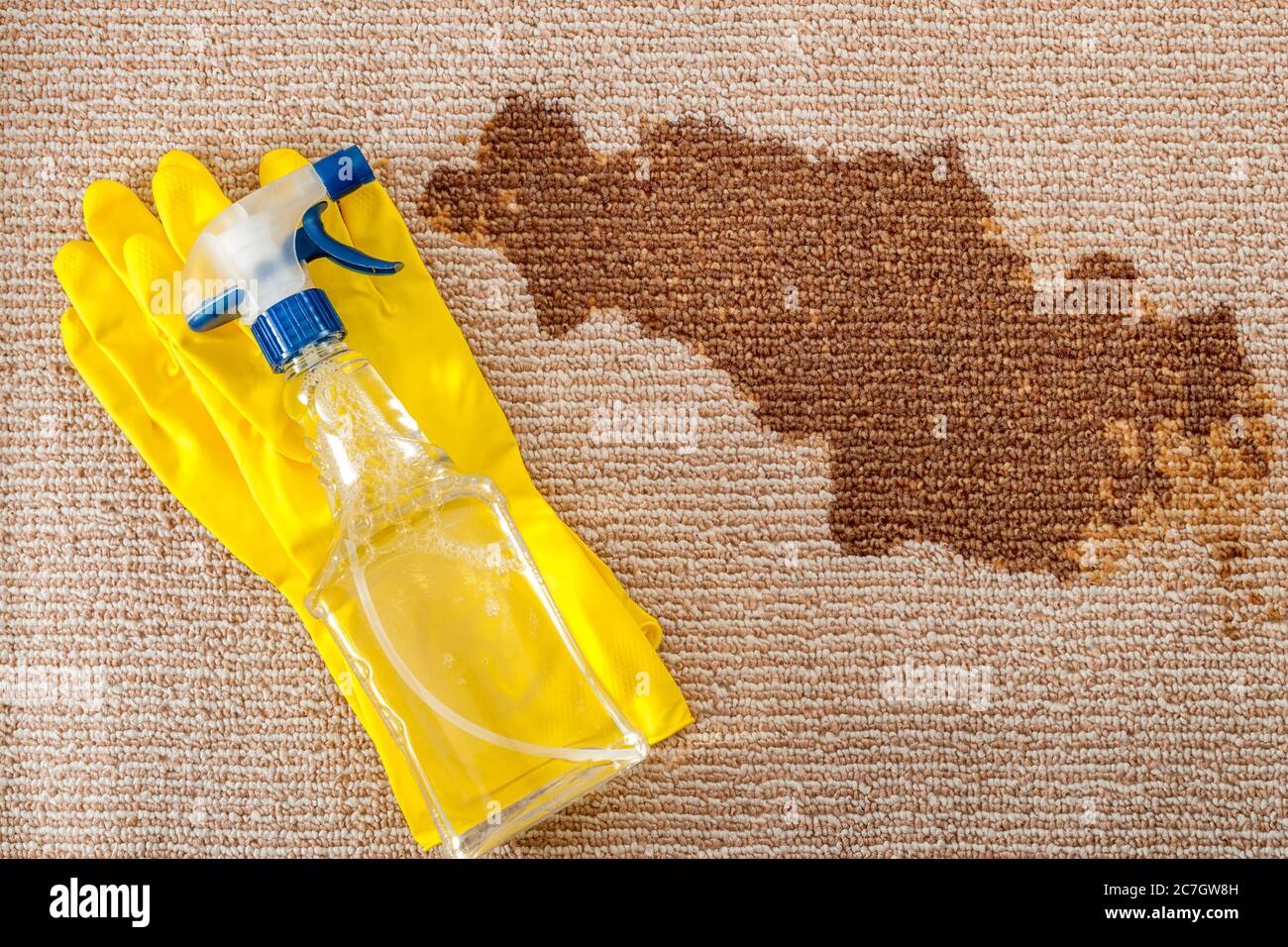 Prodotti per la pulizia e concetto di igienizzazione per tappeti con un paio di guanti in gomma gialla e una bottiglia di detergente per tappeti con una testina di spruzzatura accanto a una b asciutta Foto Stock