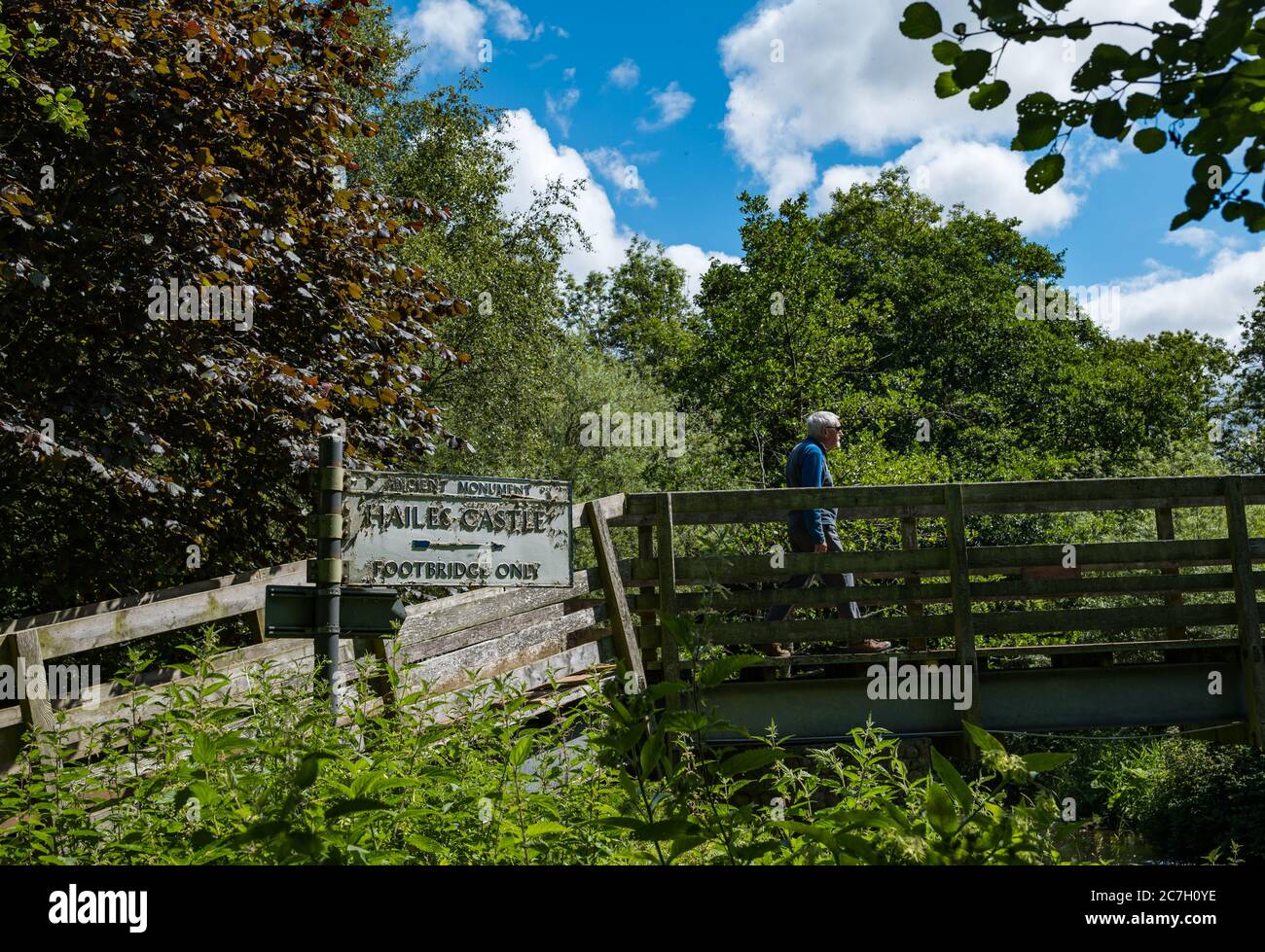 Uomo anziano che cammina sul ponte pedonale di legno con indicazione per il sentiero verso il castello di Hailes sul fiume Tyne, East Lothian, Scozia, Regno Unito Foto Stock