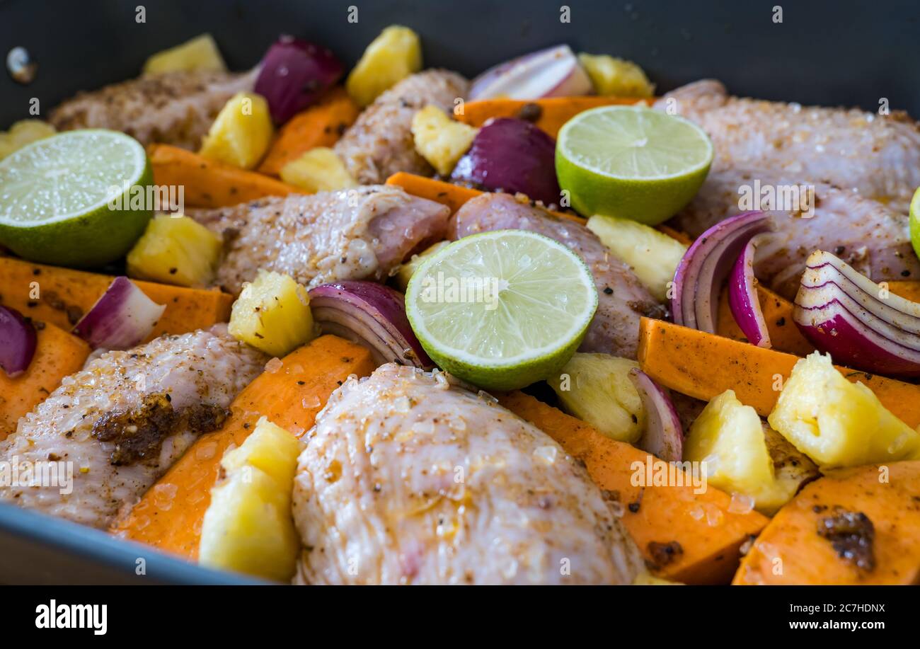 Cosce di pollo e bacchette da pollo a jerk cuocere in teglia per tostare le verdure: Patate dolci, cipolle rosse, pezzi di lime e ananas Foto Stock