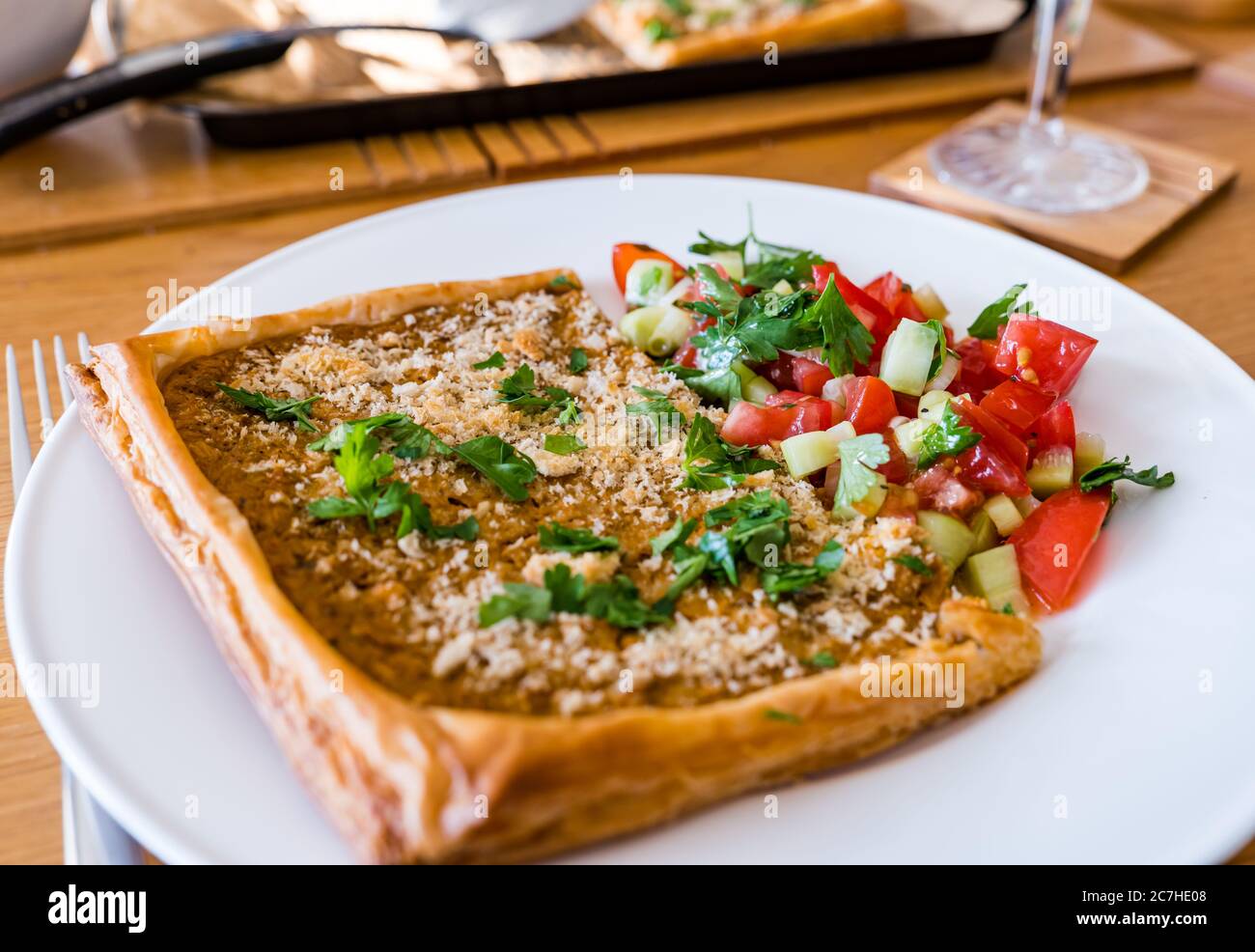 Crostata con formaggio spalmato su pasta sfoglia; cosparsa di pangrattato, parmigiano e prezzemolo, servita su piatto bianco con salsa di pomodoro Foto Stock