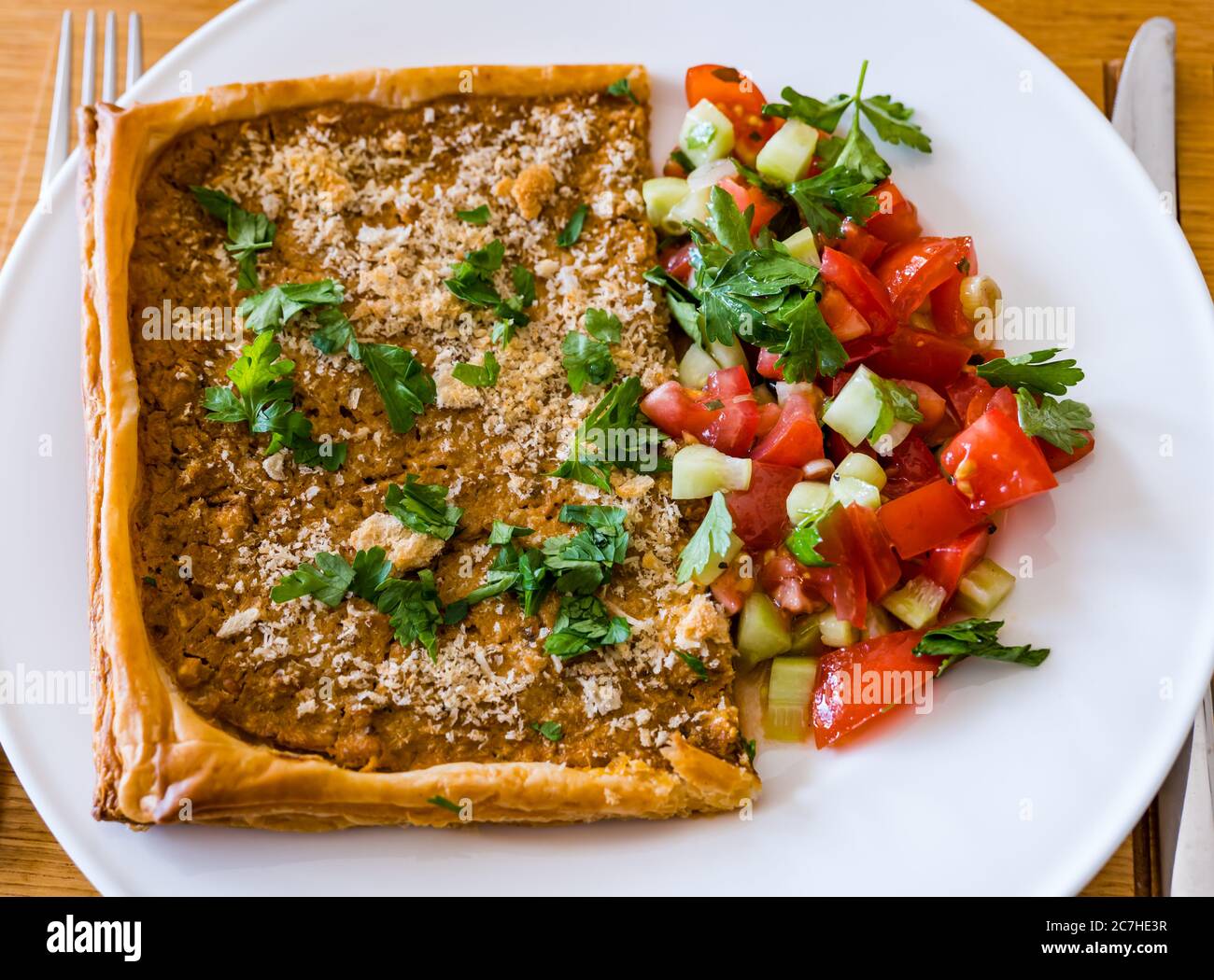 Crostata con formaggio spalmato su pasta sfoglia; cosparsa di pangrattato, parmigiano e prezzemolo, servita su piatto bianco con salsa di pomodoro Foto Stock