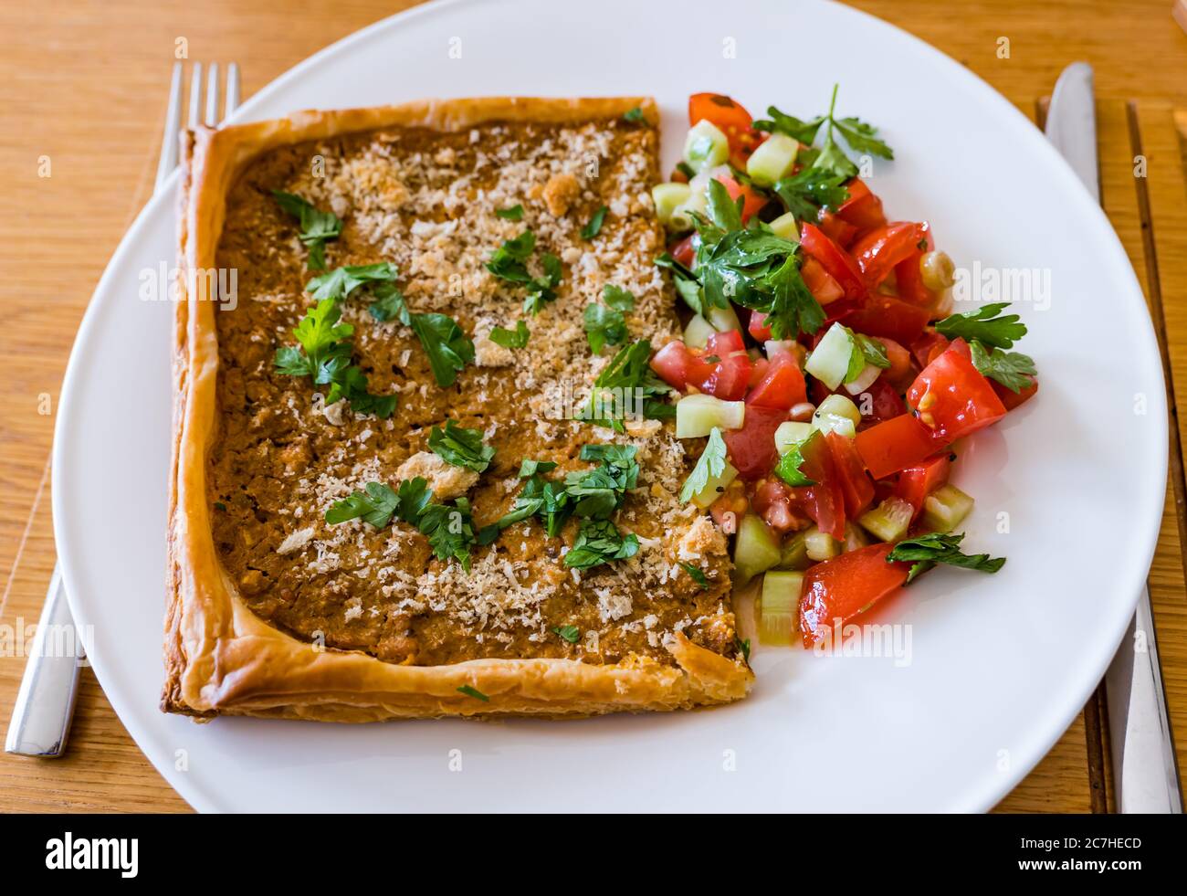 Crostata con formaggio spalmato su pasta sfoglia; cosparsa di pangrattato, parmigiano e prezzemolo, servita su piatto bianco con salsa di pomodoro Foto Stock