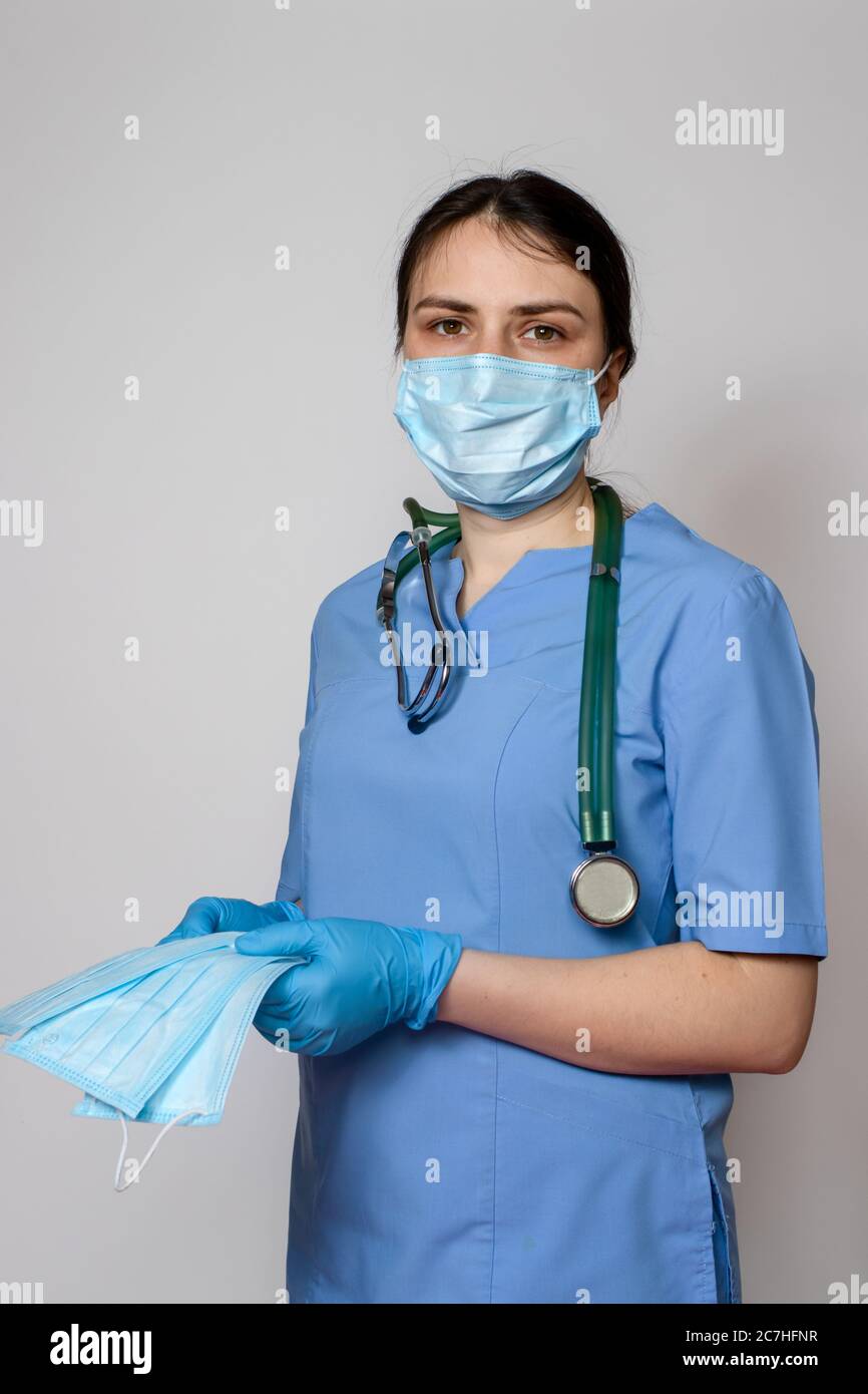 Un medico in una maschera medica e uniforme blu contiene molte maschere mediche di protezione. Foto Stock