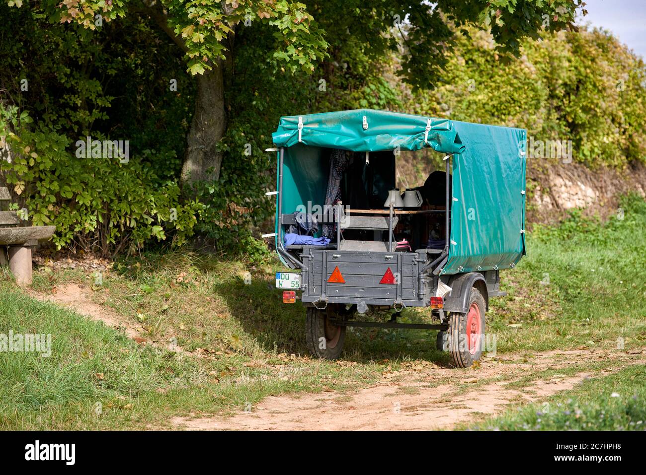 Rimorchio monoassiale con telone verde e caffettiera davanti alla parete del vigneto Foto Stock