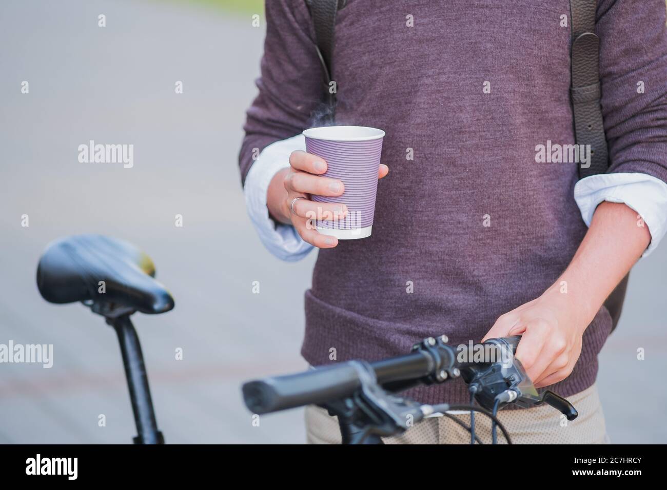 Tazza di caffè caldo nelle mani di un pendolarello per biciclette. Andare a lavorare in bicicletta, concetto di stile di vita urbano attivo Foto Stock