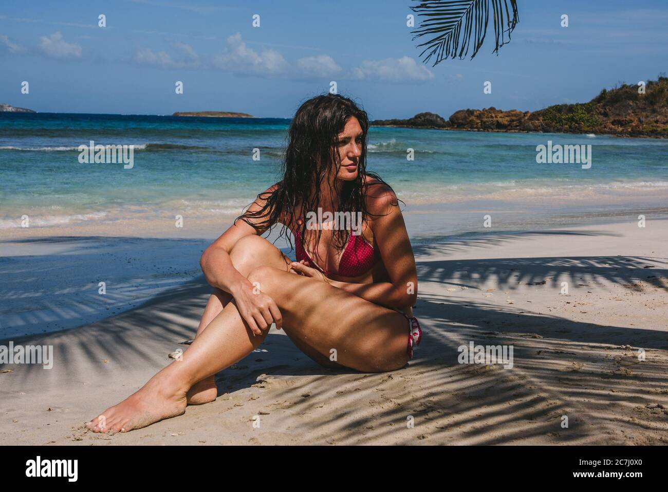 Una donna seduta nella sabbia di Zoni Beach all'ombra di una palma a Culebra, Puerto Rico Foto Stock