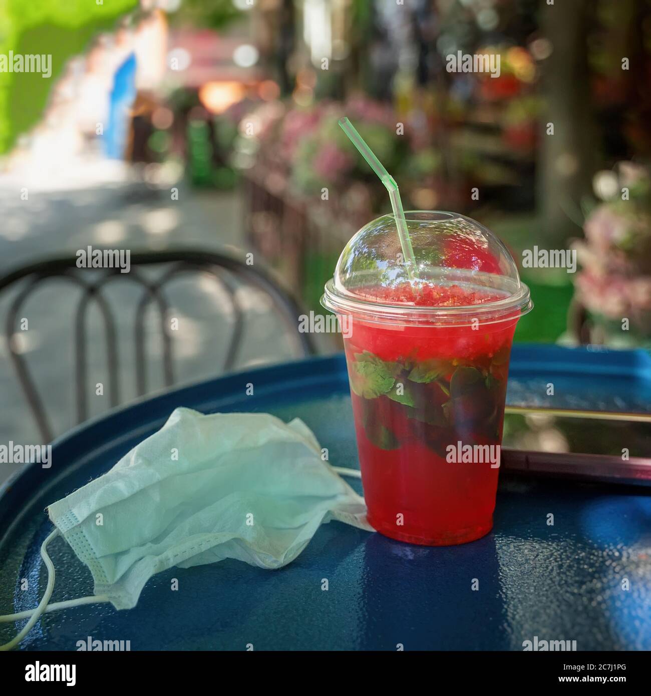Tazza di plastica usa e getta con bevanda rinfrescante e maschera medica protettiva, tavolino Street cafe, terrazza, estate. Nuove misure di normalità e sicurezza Foto Stock