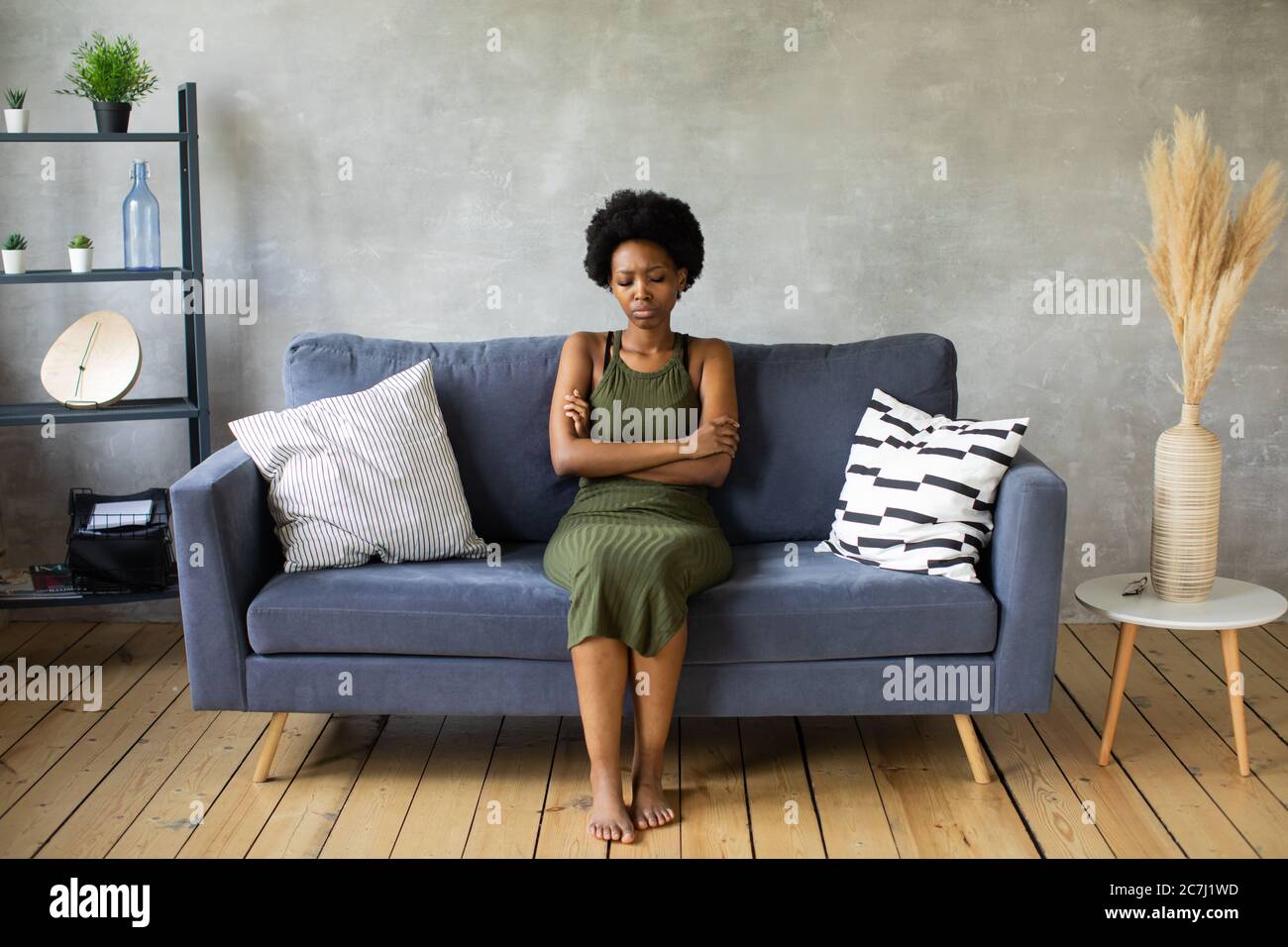 Infelice donna afroamericana siediti sul divano, la ragazza è molto turbata seduta sul divano del suo appartamento. Foto Stock