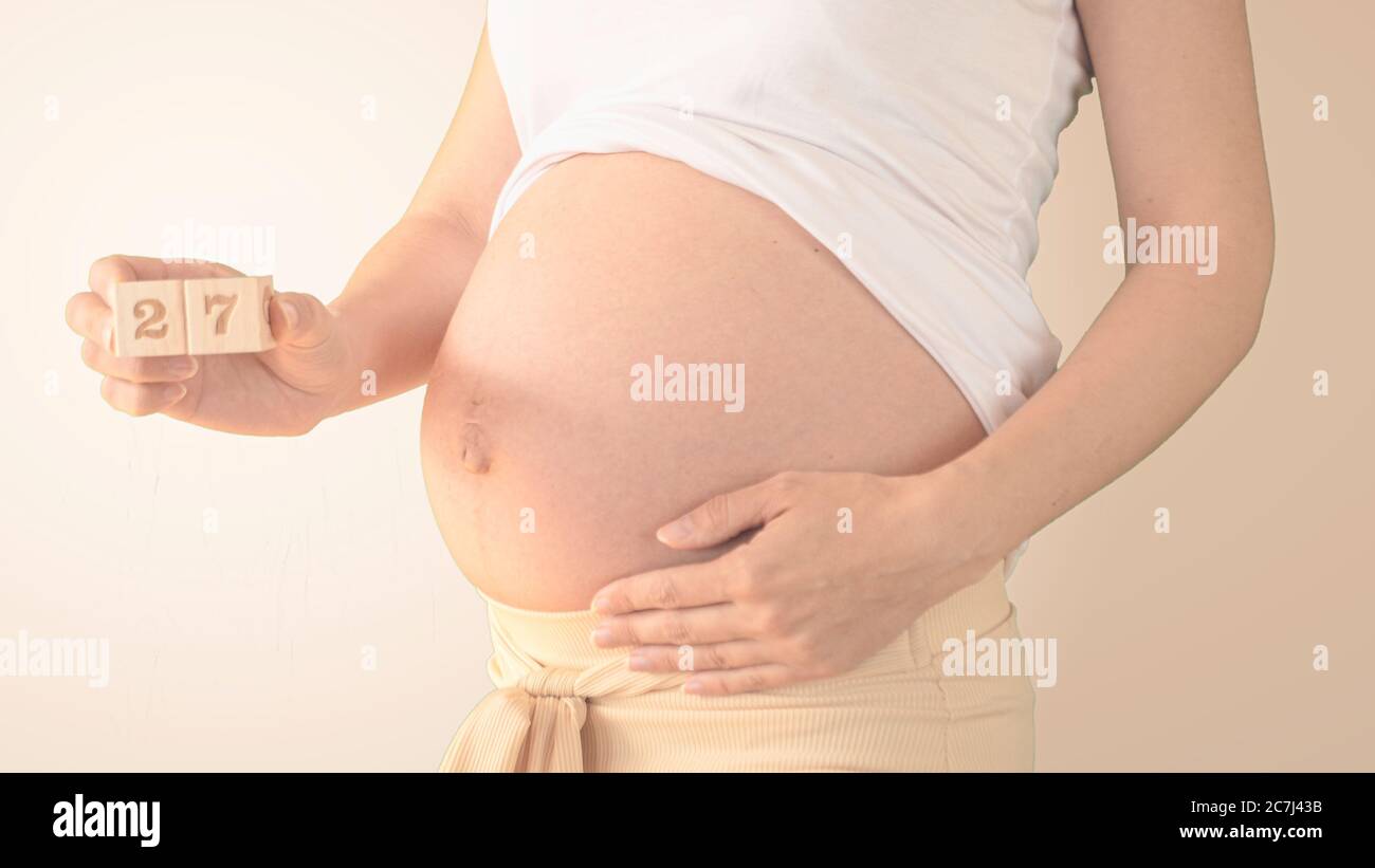 Giovane donna incinta con numero di settimana di gravidanza accanto alla pancia. Foto della crescita della pancia a 27 settimane di gravidanza. Dieta sana di gravidanza Foto Stock