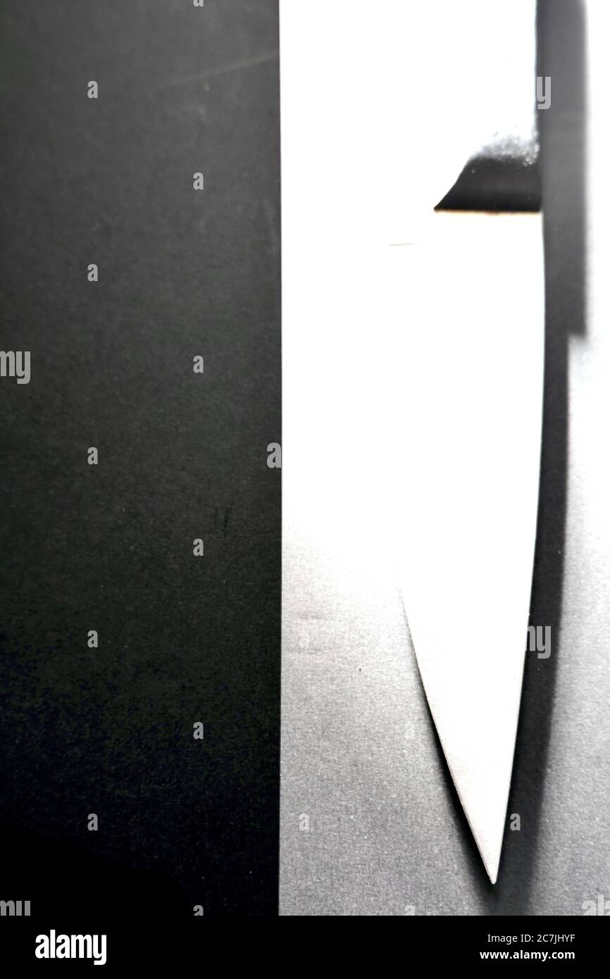 Immagine verticale in scala di grigi di un coltello su un nero e superficie bianca catturata da un angolo elevato Foto Stock