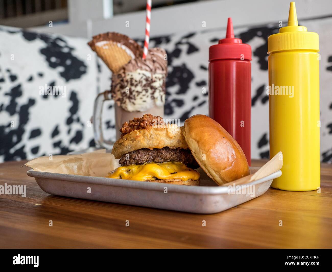 Burger su un vassoio con ketchup e senape vicino a. frullato di cioccolato su un tavolo di legno Foto Stock
