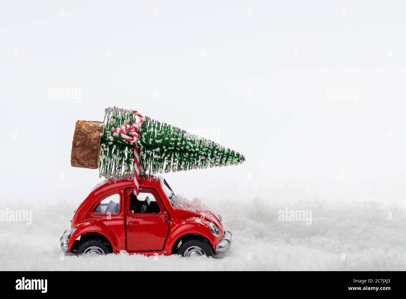Il modello di auto rossa trasporta il mini albero di Natale, neve artificiale, sfondo bianco, Foto Stock