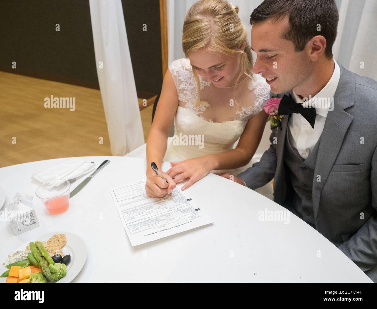 Coppia appena sposata che firma un documento di potenup su un tavolo bianco sotto le luci Foto Stock