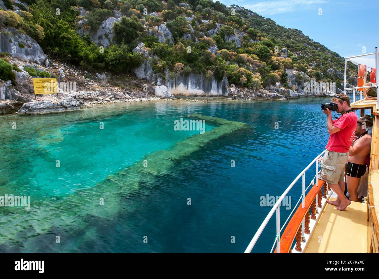 Una barca turistica che si trova accanto a una sezione della città di Sunken al largo dell'isola di Kekova, nella regione mediterranea occidentale della Turchia. Foto Stock