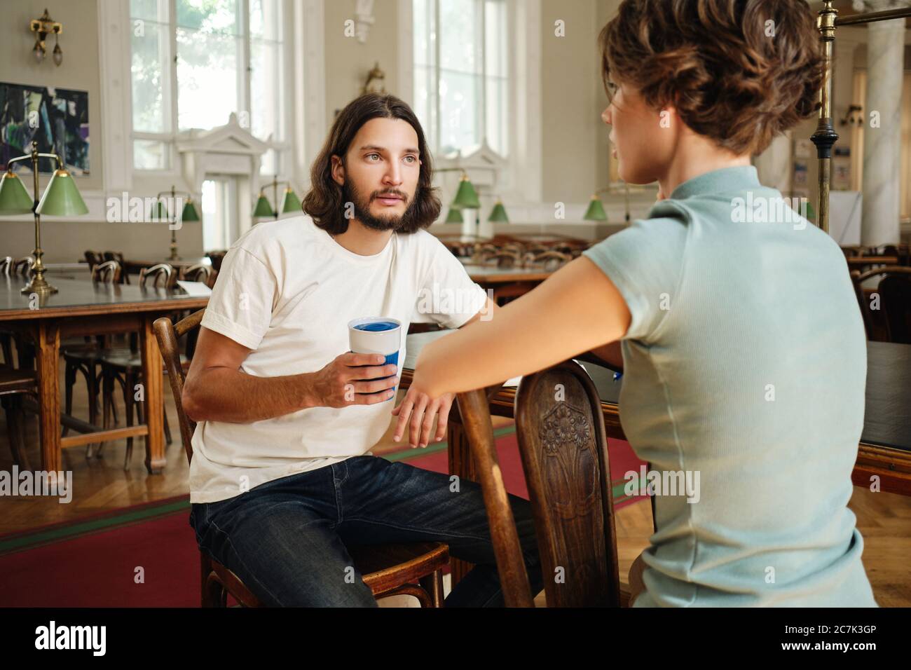 Giovane studente di sesso maschile che parla con un amico durante lo studio in biblioteca di università Foto Stock