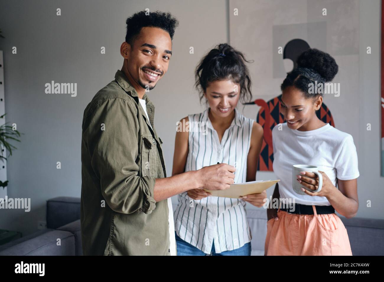 Giovane afroamericano che guarda felicemente in macchina fotografica durante il lavoro con i colleghi in uno spazio di lavoro di cooperazione Foto Stock