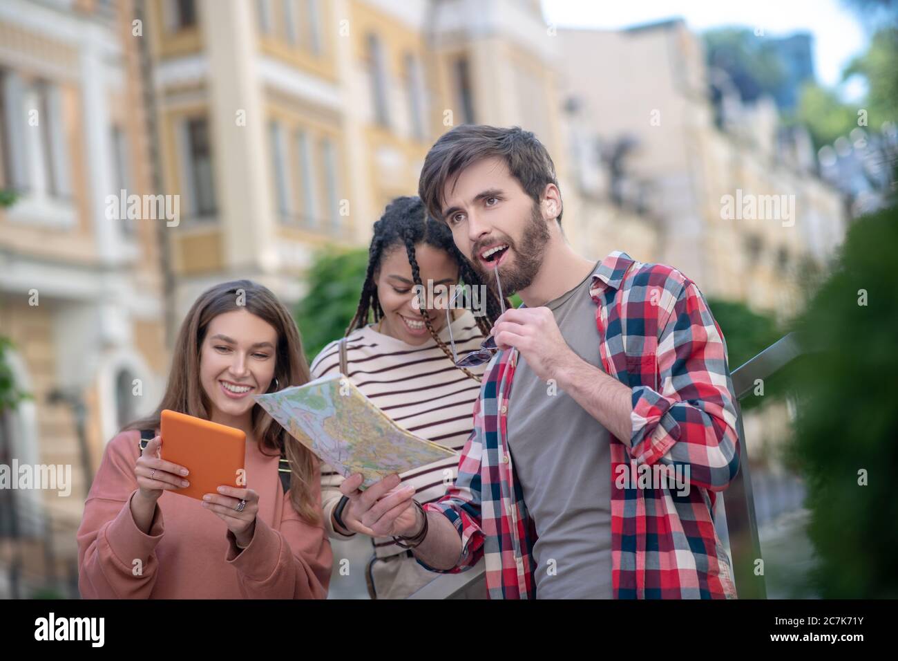Ragazzo sorpreso e gioioso con mappa e due ragazze con tablet Foto Stock