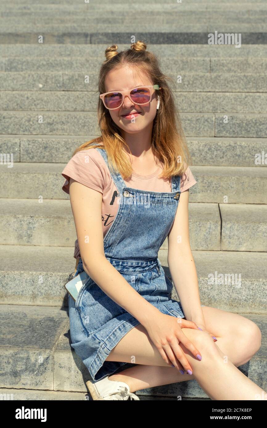 bella giovane ragazza con capelli rossi in occhiali da sole si siede sui  gradini di pietra e sorride sinceramente Foto stock - Alamy