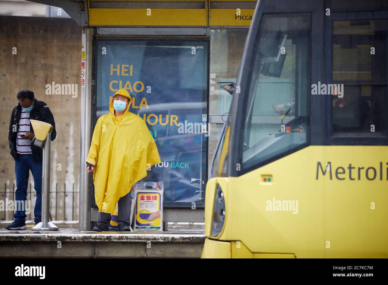 I passeggeri della stazione del tram Metrolink dei Manchester Piccadilly Gardens indossano maschere che aspettano il loro tram Foto Stock