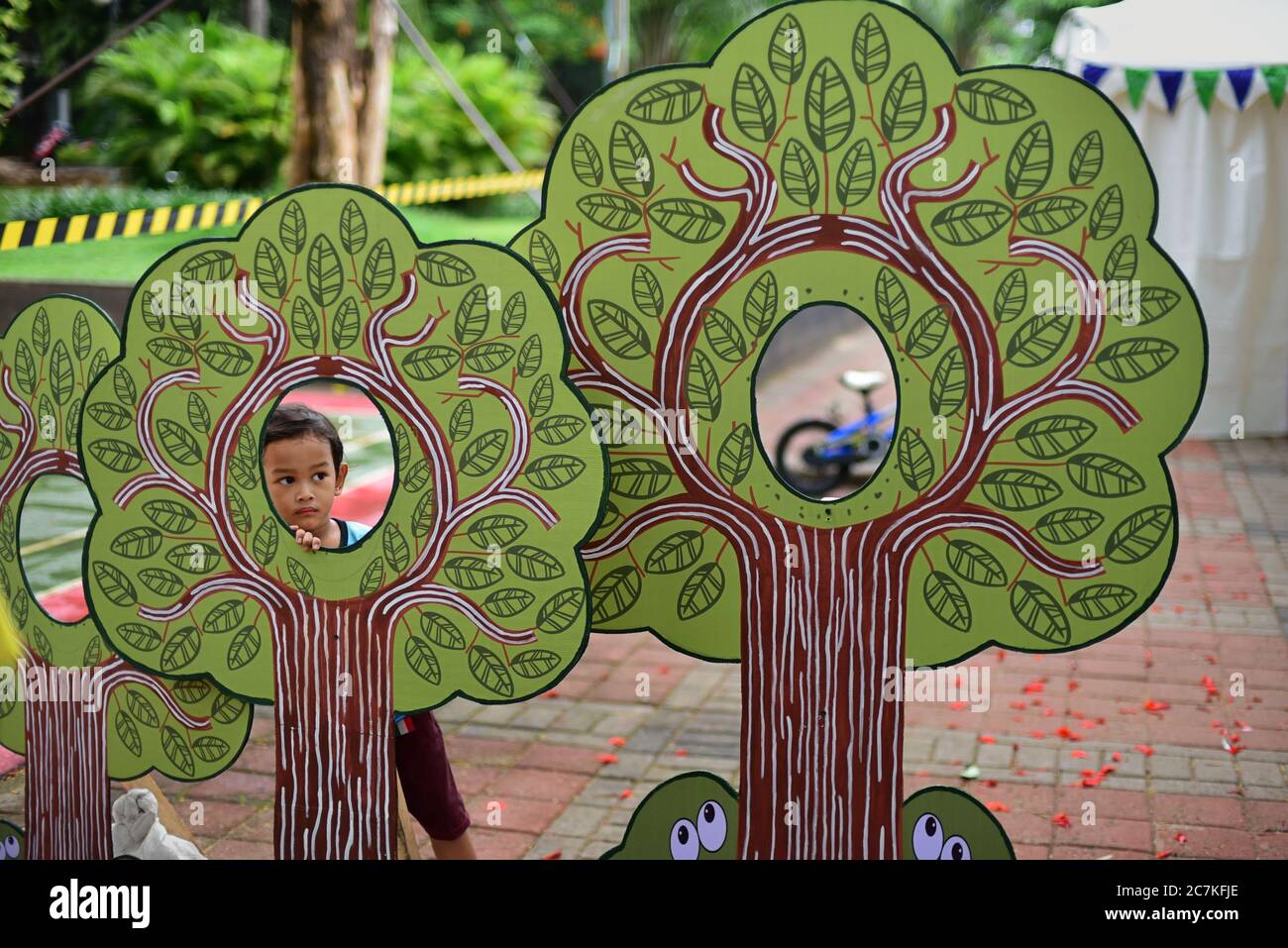 Un bambino che guarda attraverso le tavole ad albero, decorazione ambientale all'aperto durante un evento pubblico tenuto da Greenpeace a Giacarta, Indonesia. Foto Stock