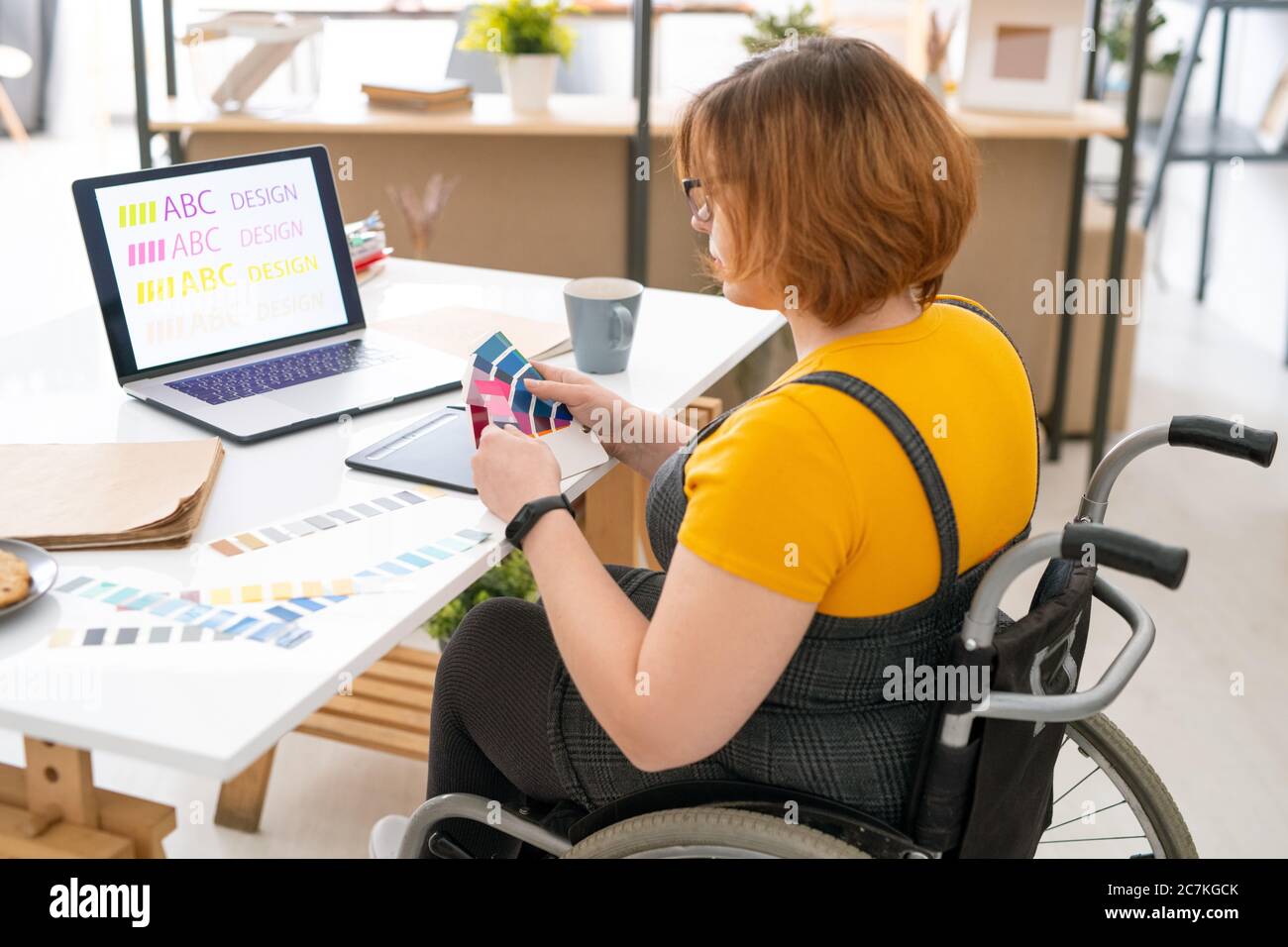 Designer giovane grazioso in casualwear seduto da lavoro in ambiente domestico e la scelta del colore per il sito web design dalla tavolozza Foto Stock