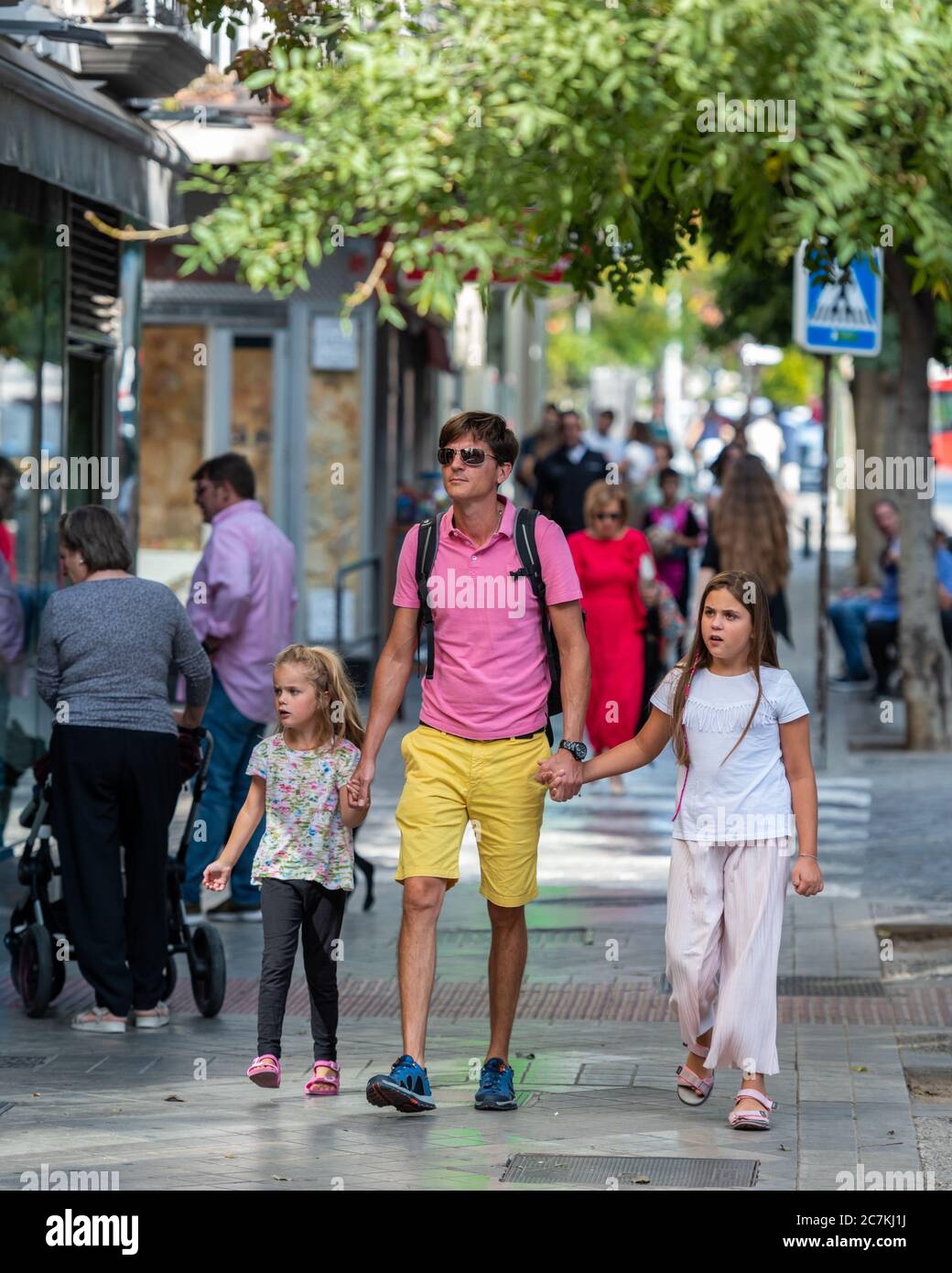 Un padre colorato e le sue due giovani figlie che si godono una gita di sabato in Calle San Juan de Dios, Granada§ Foto Stock