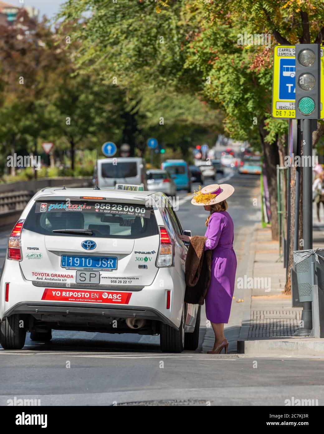 Una donna in un grande cappello di paglia che salutava un taxi In una strada alberata a Granada Foto Stock