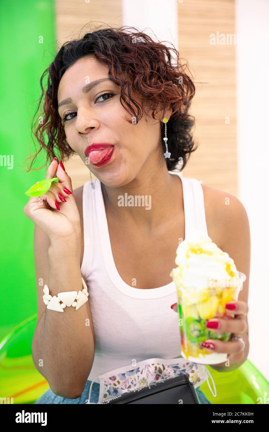 Ritratto di una donna latino-americana che assaggia felicemente un gelato. Messa a fuoco selettiva. Concetto di estate e stile di vita. Foto Stock